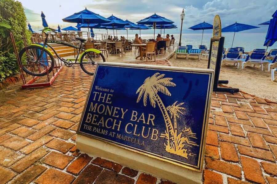 A rustic sign marks the entrance to a lively beach club, inviting visitors to enjoy food, drinks, and fun.