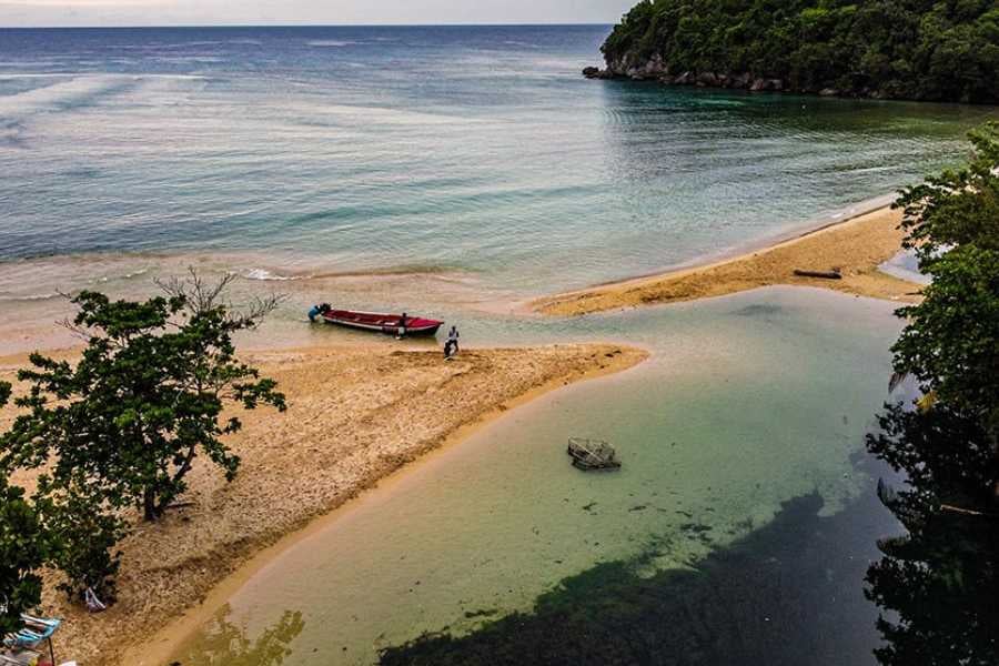 A quiet inlet meets the ocean, where a red boat rests on golden sand surrounded by lush green hills.