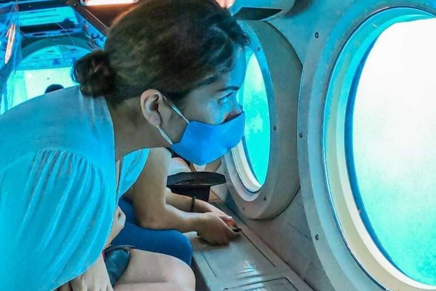 A woman peers through the windows of a submarine, gazing at the deep blue sea with curiosity.