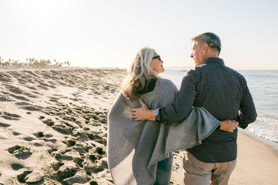 A couple enjoys a peaceful walk along a sunny beach, wrapped in cozy blankets and warm conversation.