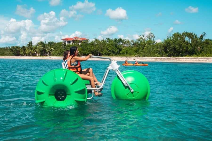 Two friends pedal a giant floating bike on the calm, clear waters of a tropical lagoon.