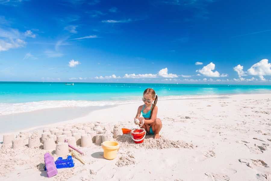 A girl is sitting on the white sand and playing