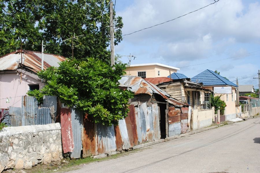 A quiet Jamaican neighborhood with old tin-roof houses along a narrow street.