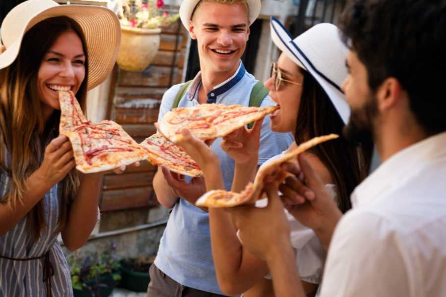 Friends laughing and enjoying giant slices of pizza outdoors, creating a fun and casual dining experience.