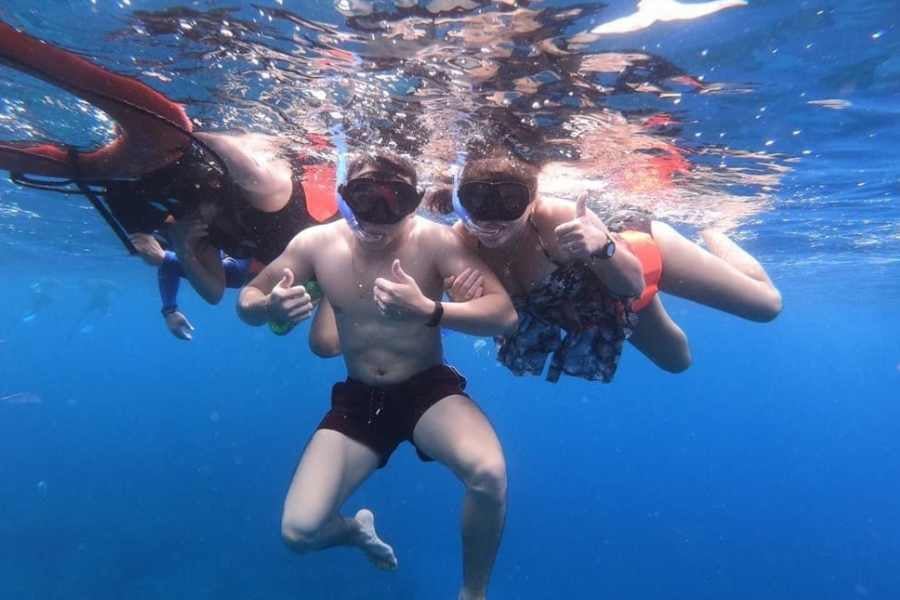 A group of snorkelers poses underwater, giving thumbs-up signs as they explore the marine world.