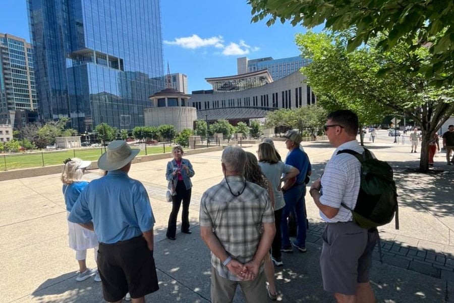 A tour guide chats with a curious group under sunny city skies.