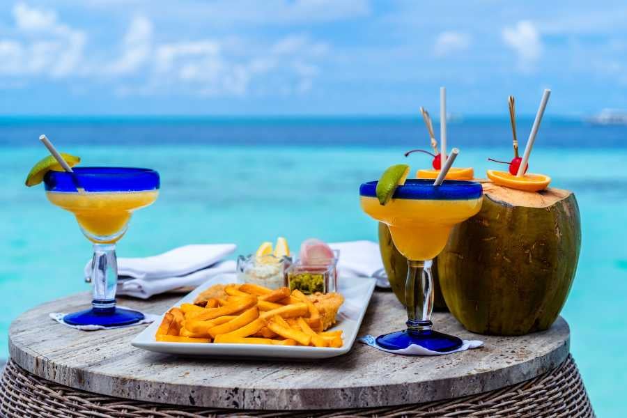 Two margaritas, fresh coconuts, and a plate of fries and fish are served with a stunning ocean view.