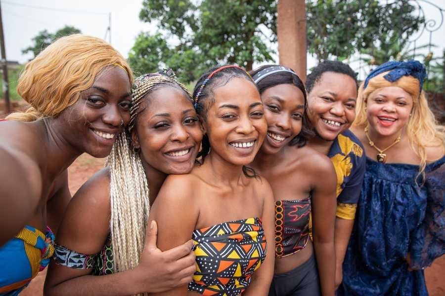 A group of smiling women pose together in bright, patterned clothing.
