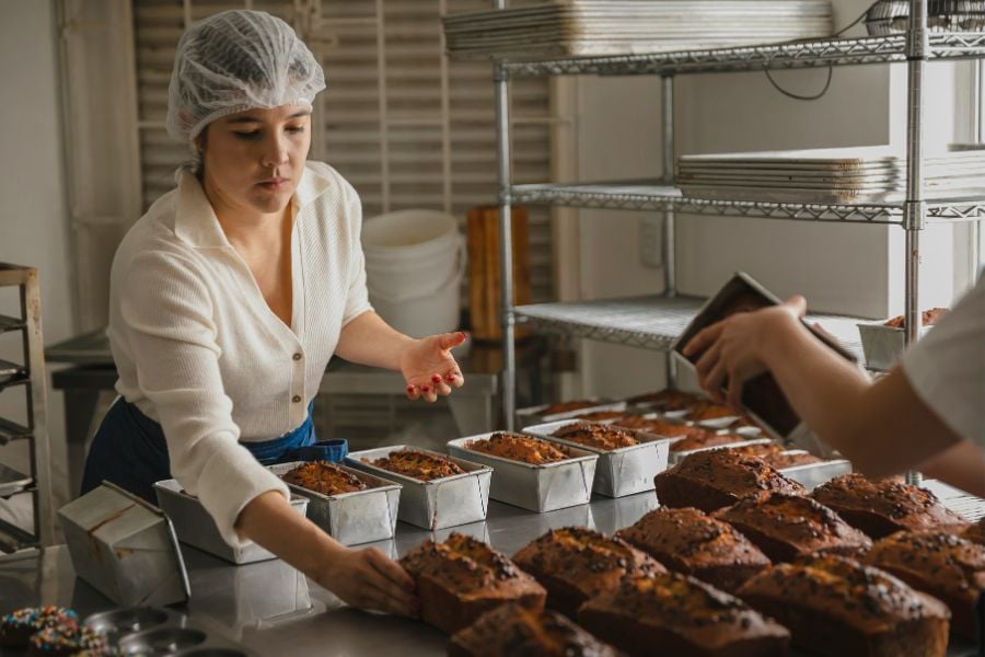 A baker arranges freshly baked loaves of bread on a kitchen counter.