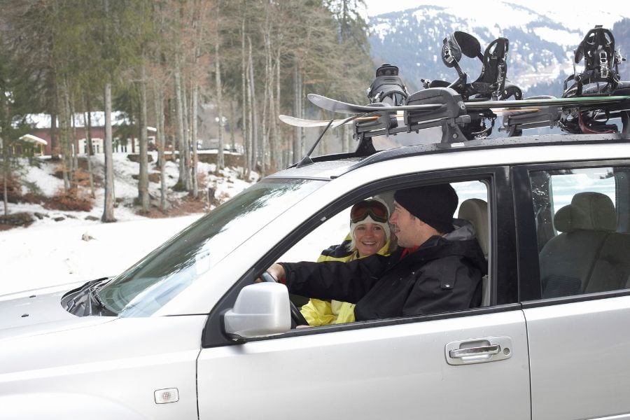 A couple in a car with skis and snowboards on the roof.