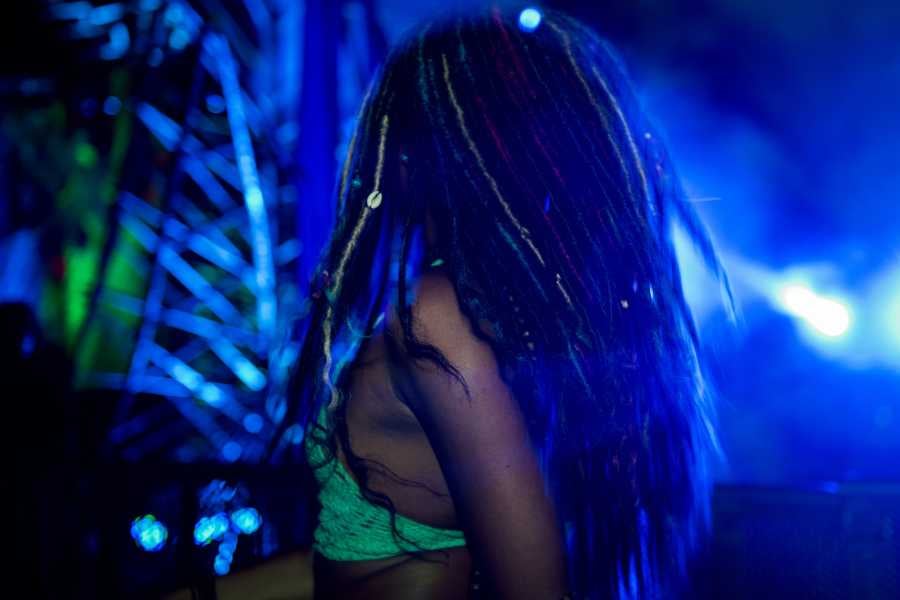 A woman dances energetically with her back to the crowd, surrounded by bright lights at a club.