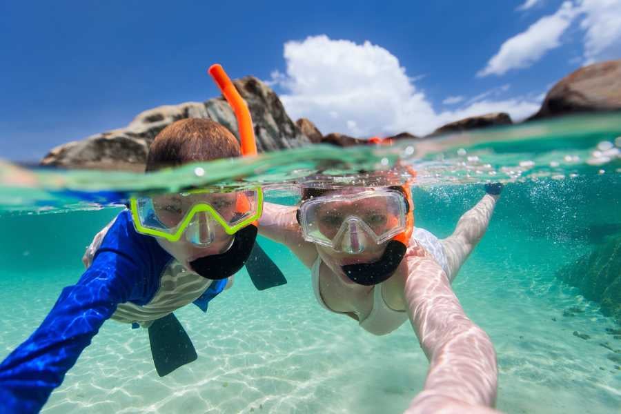 A couple snorkeling in crystal-clear turquoise waters with colorful gear, enjoying an underwater adventure.