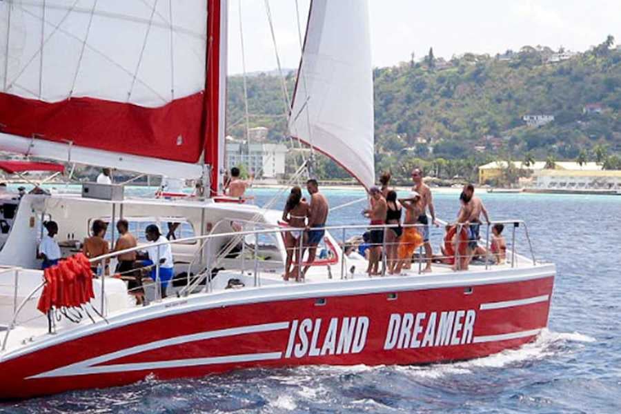 A group sails on a red catamaran, soaking up the sun and scenic coastal views on a dreamy day.