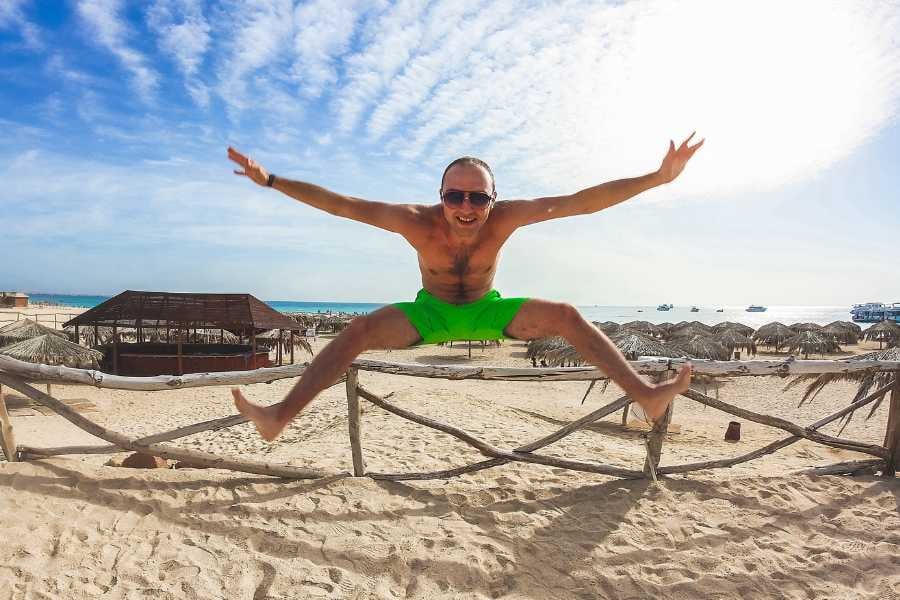 A vibrant, carefree moment as a traveler leaps joyfully at a stunning beach with a clear blue sky.