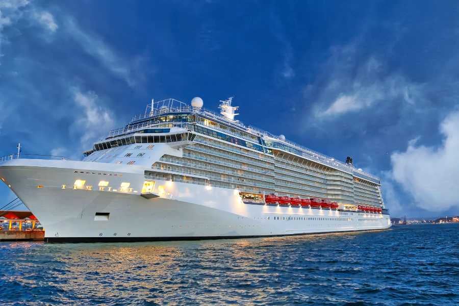 A majestic cruise ship lights up the evening sky as it docks near a picturesque harbor.