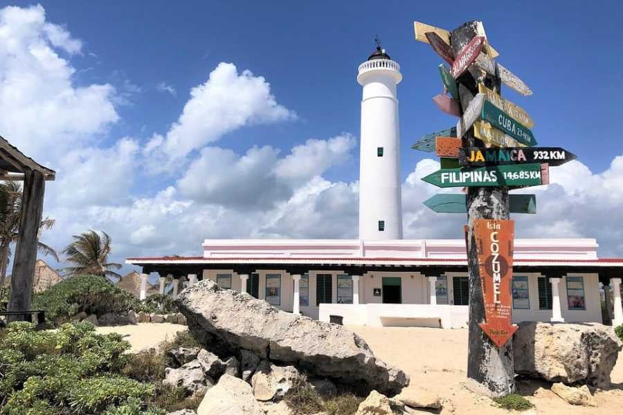 A lighthouse stands tall near a quirky signpost pointing to far-off destinations, set against a sunny coastal backdrop.