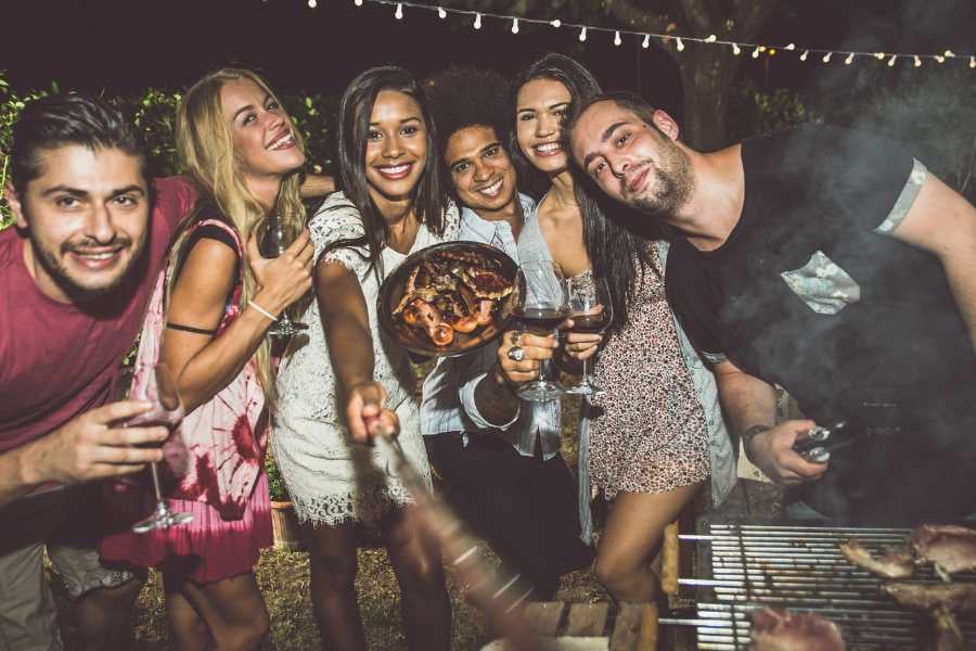 A group of friends enjoying a barbecue with grilled food and drinks under string lights.