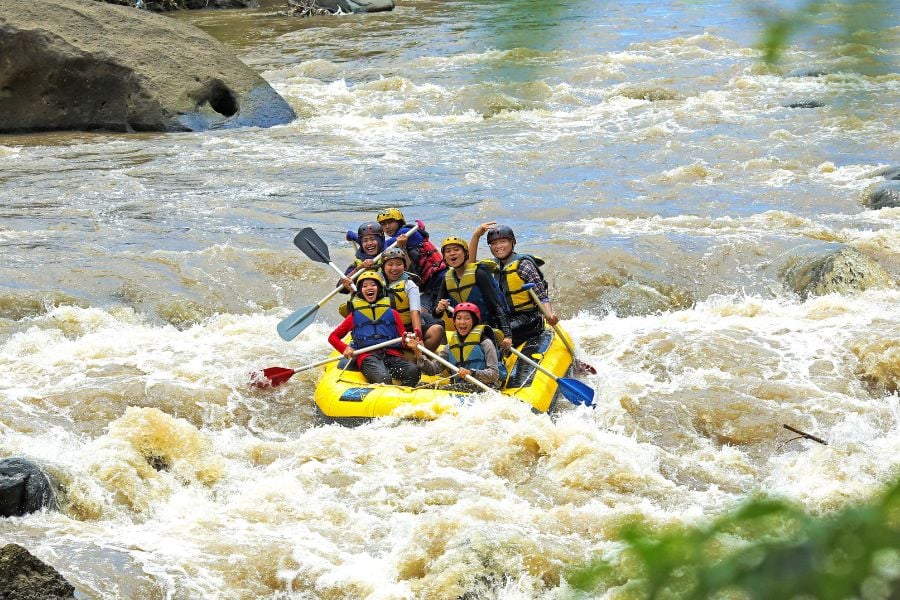 A group paddles through fast rapids, laughing as their raft bounces around.