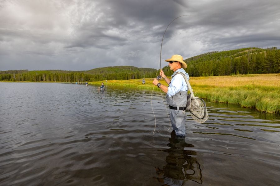 Angler in straw hat casts as storm clouds gather over Yellowstone waters.