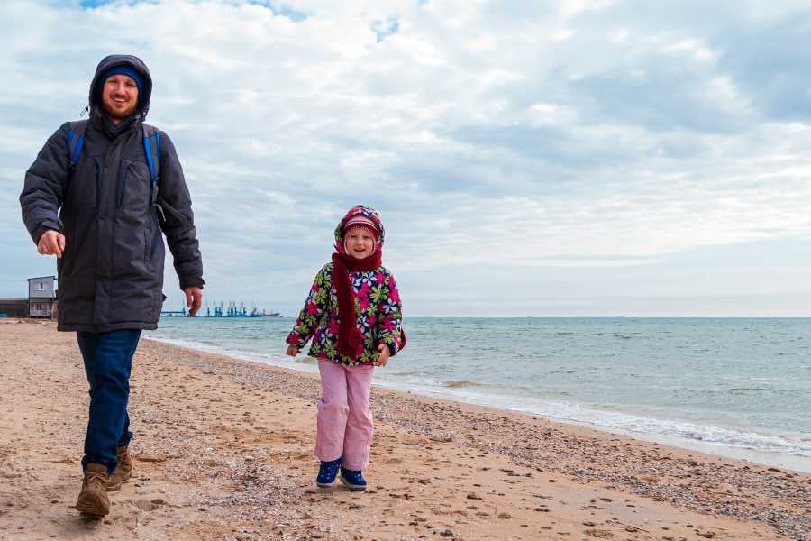 A parent and child enjoy a chilly walk on the beach, dressed in warm clothes.