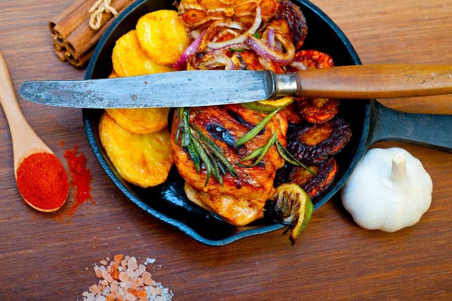 A sizzling skillet of grilled chicken, roasted plantains, and vegetables, seasoned with aromatic herbs and spices.