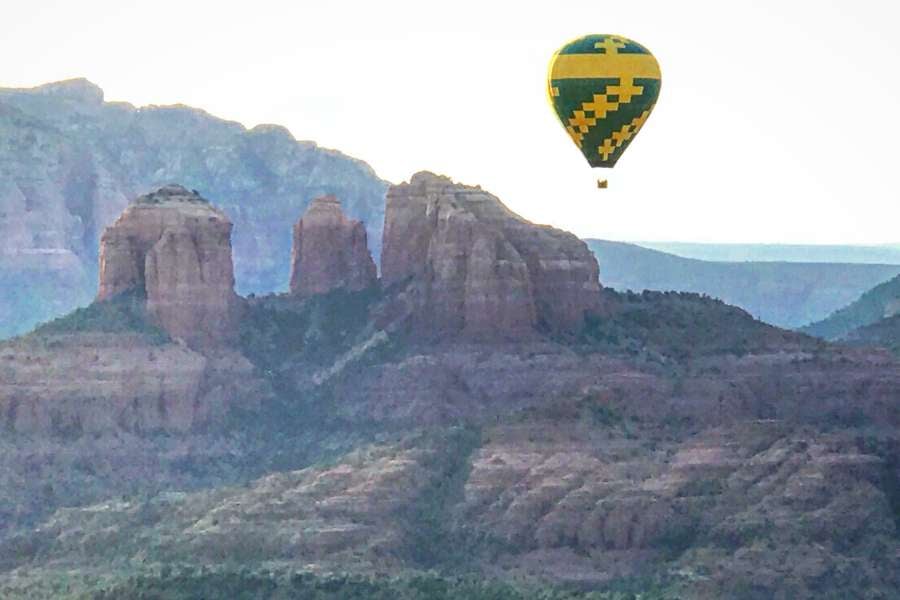 A colorful hot air balloon floats above tall red rock formations at sunset.