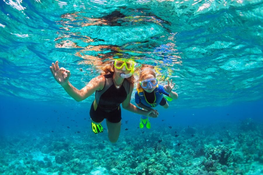 Two people snorkel happily in clear blue water above a colorful reef.