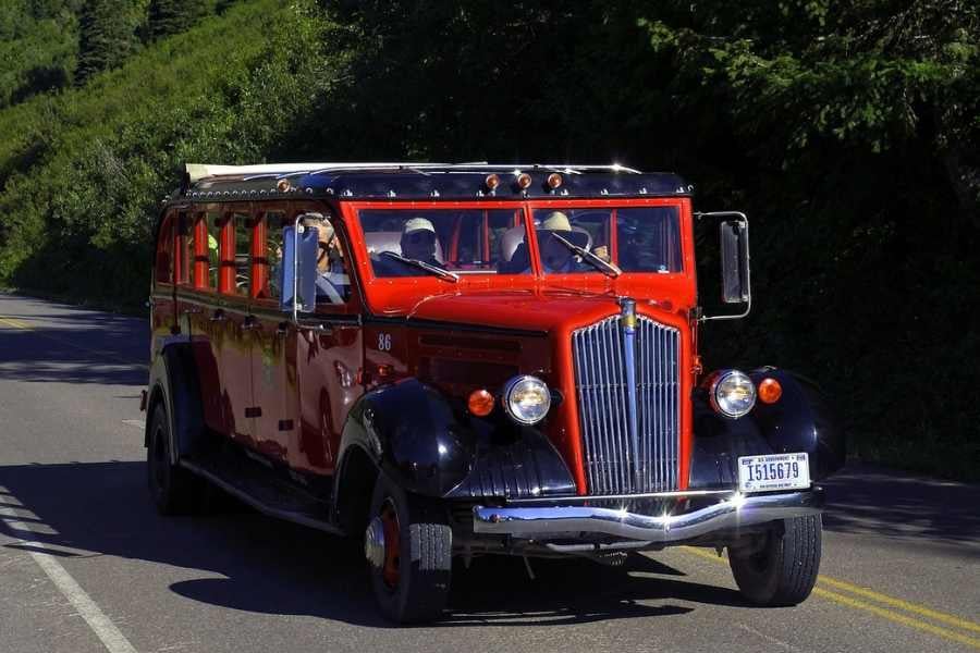 An iconic red bus traversing scenic mountain roads with passengers aboard.
