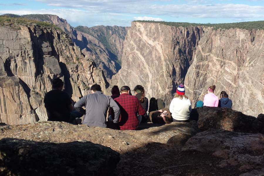 people sitting top of cliff overlooking canyon