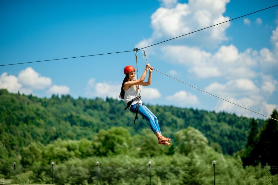 Woman gliding joyfully across a forest zipline on a sunny day.