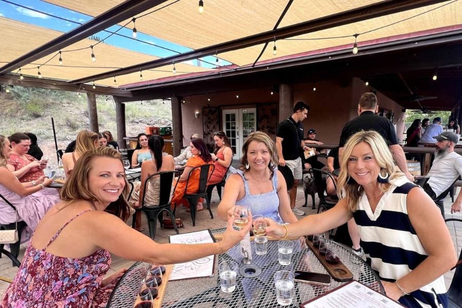 Three friends raise their glasses at a lively outdoor tasting event.