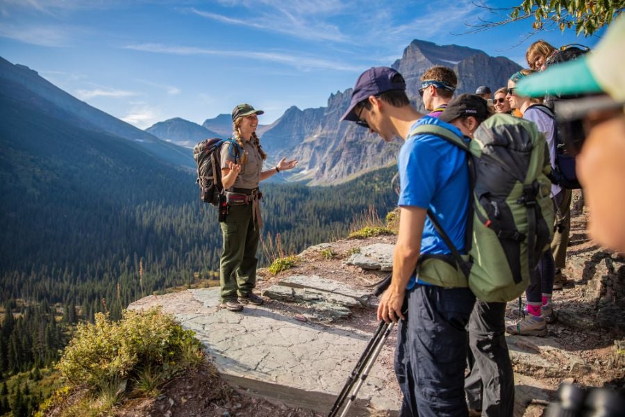 A ranger leads a group of hikers along a cliffside trail with sweeping views.