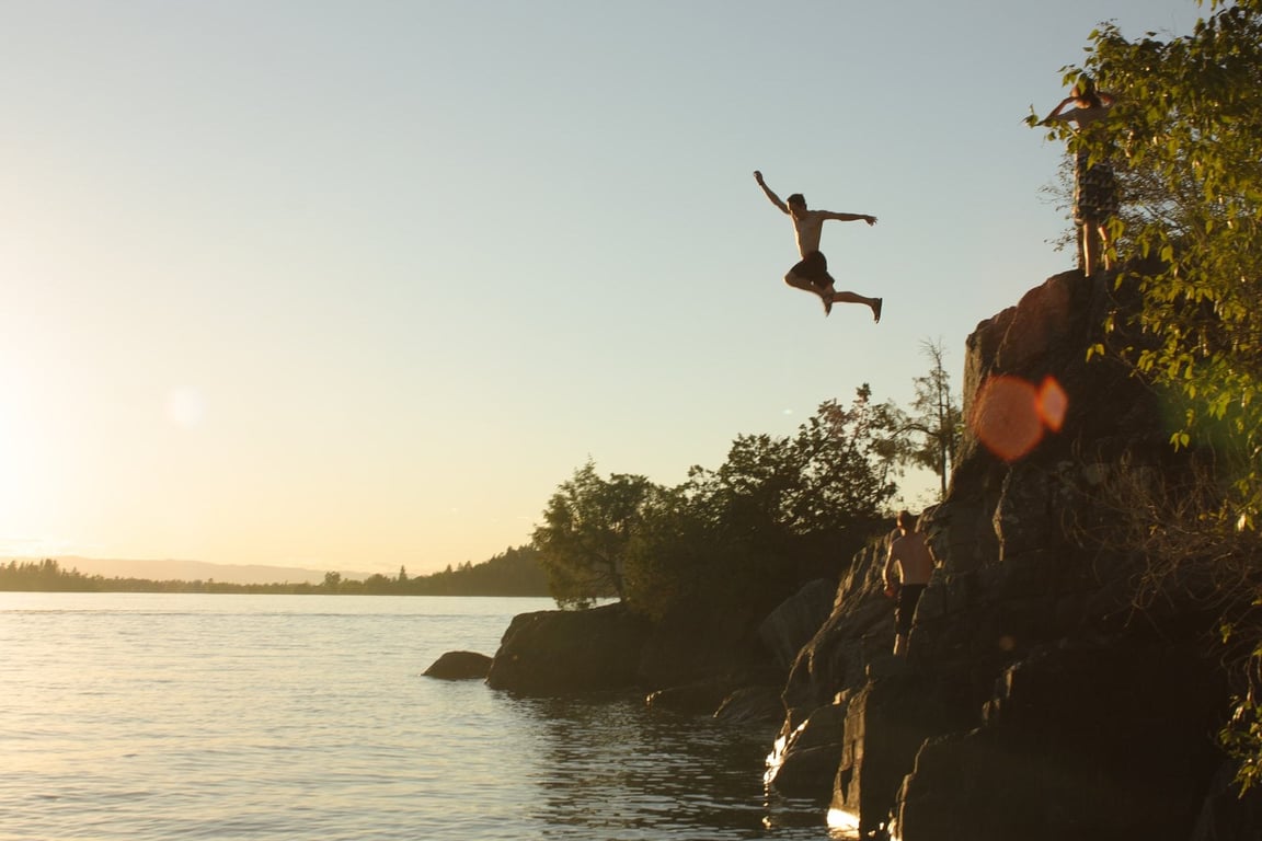 man jumping from cliff into lake