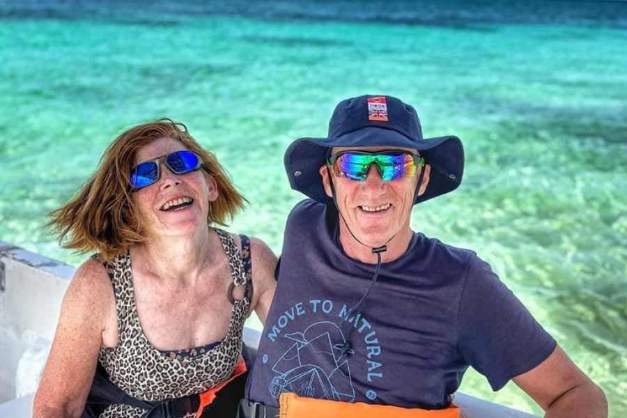 A smiling couple relaxes on a boat, enjoying the sun and the breathtaking turquoise waters behind them.