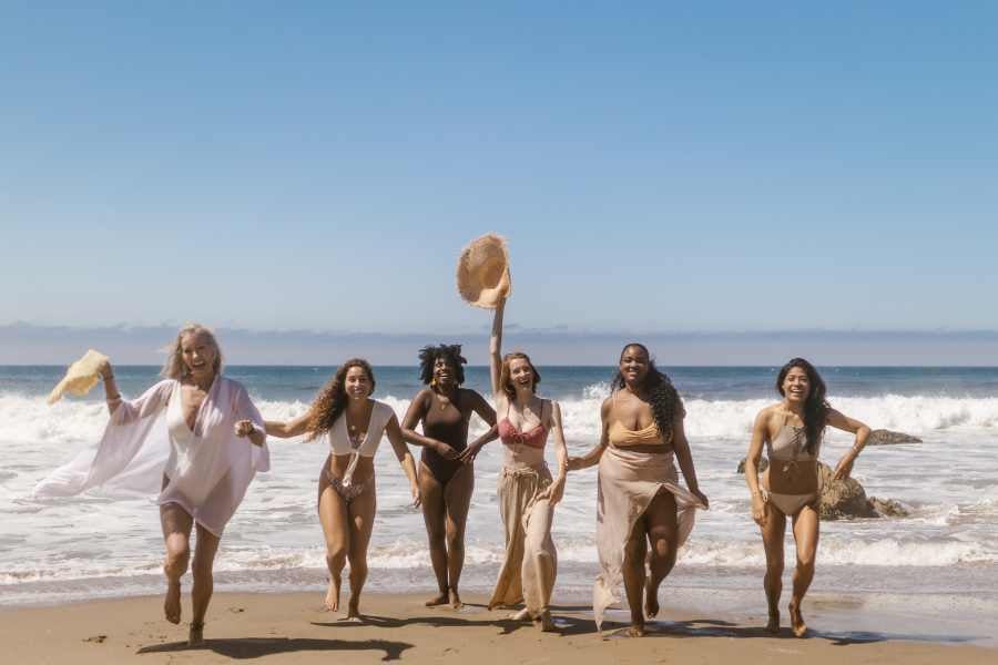 Group of friends laughing and running along a sunny beach, celebrating a perfect day by the sea.