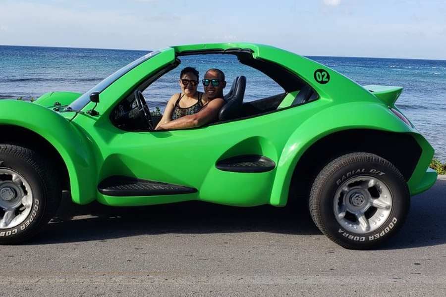 A couple cruises the coastline in a bright green dune buggy, enjoying the ocean breeze and scenic views.