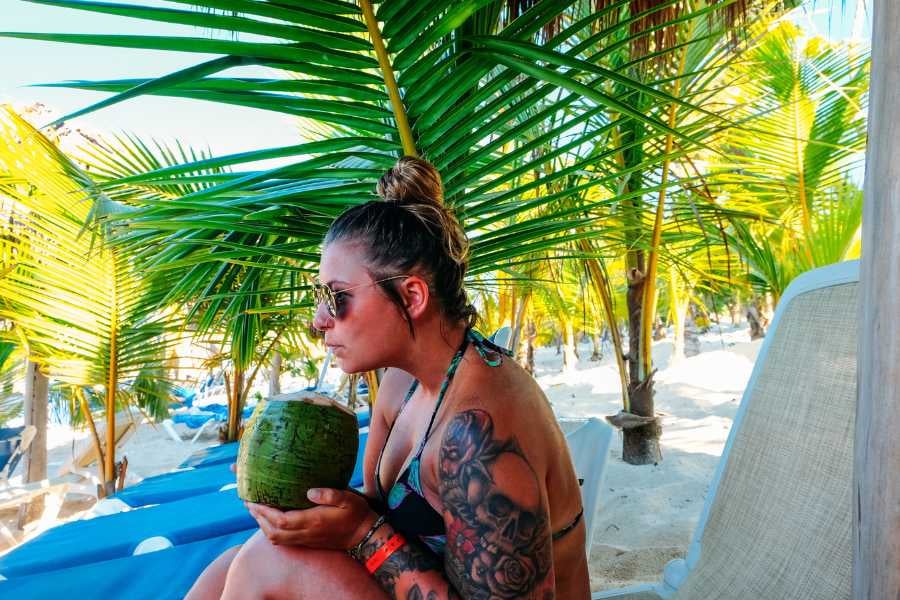 A woman savoring fresh coconut water under lush palm trees at a sunlit beach.