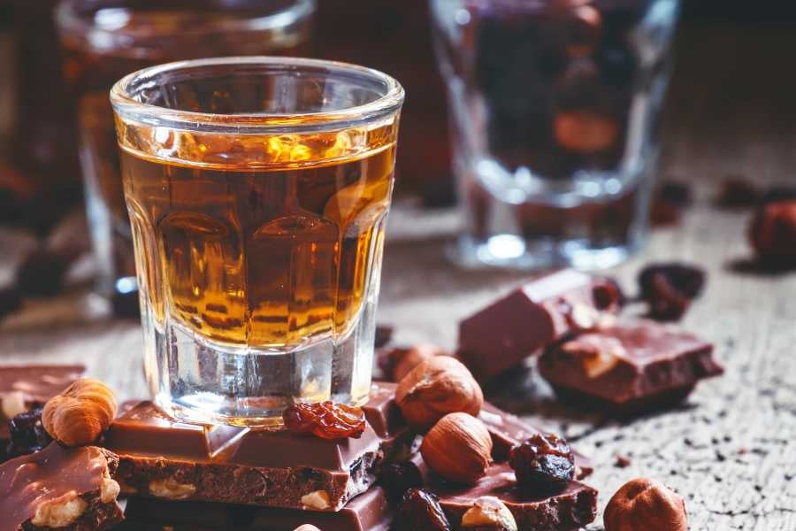 A glass of golden rum sits beside rich chocolate and nuts, creating a perfect pairing of flavors and indulgence.