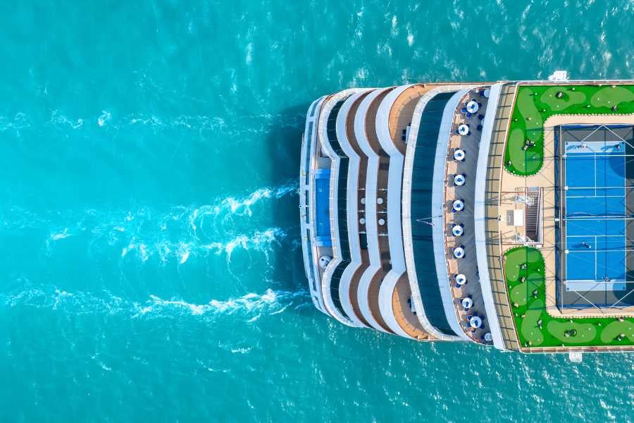 A luxurious cruise ship sails through crystal-clear turquoise waters, leaving behind gentle waves in its wake.