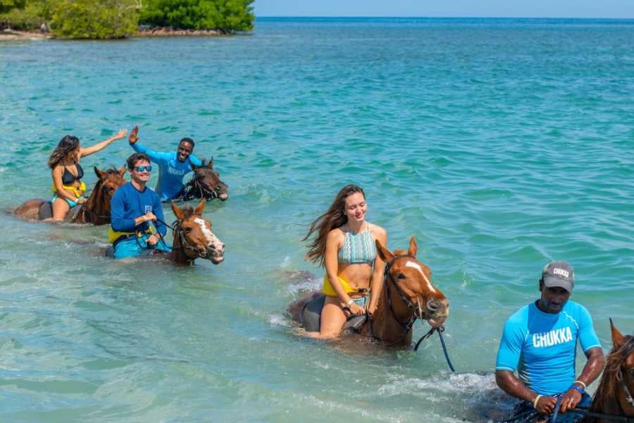 Riders guide their horses through crystal-clear ocean waters, enjoying an unforgettable beach adventure.