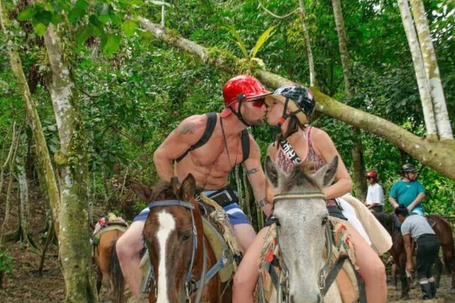 A couple on horseback, sharing a sweet kiss while exploring a lush jungle trail.