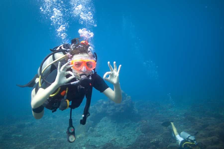 A scuba diver signals "OK" underwater in crystal-clear water.