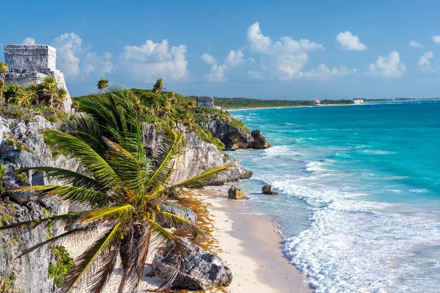 Stunning coastal view with ancient Mayan ruins overlooking a pristine white-sand beach and turquoise sea.