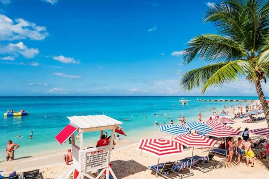 A lively beach scene with colorful umbrellas, crystal-clear water, and a lifeguard station.