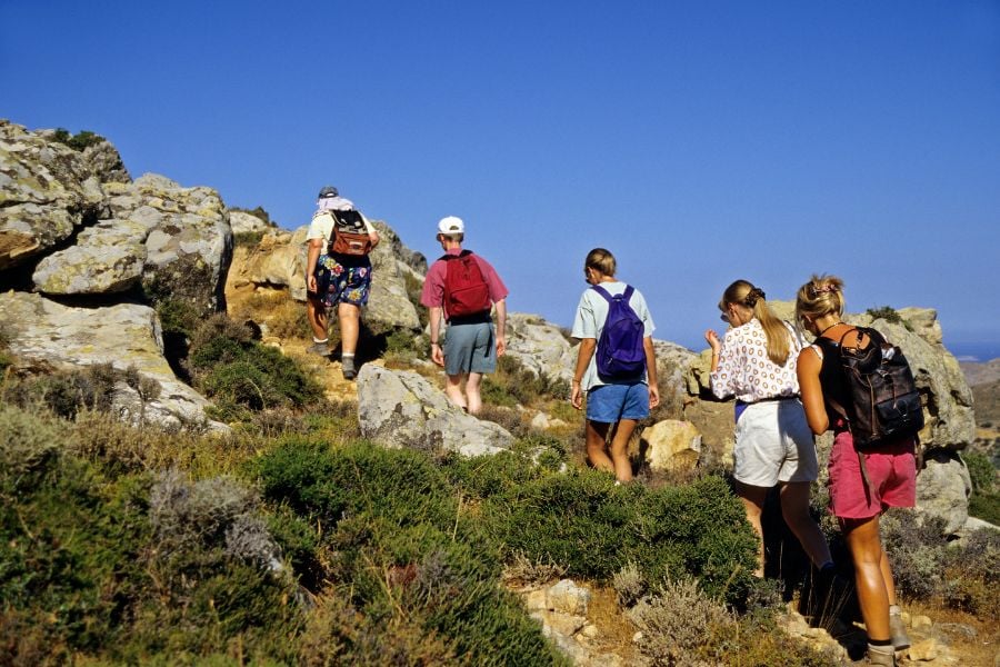Group hiking together across rocky terrain under a bright blue sky.