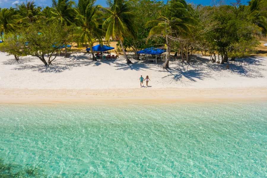 Couple strolling hand-in-hand along a peaceful beach with clear water.