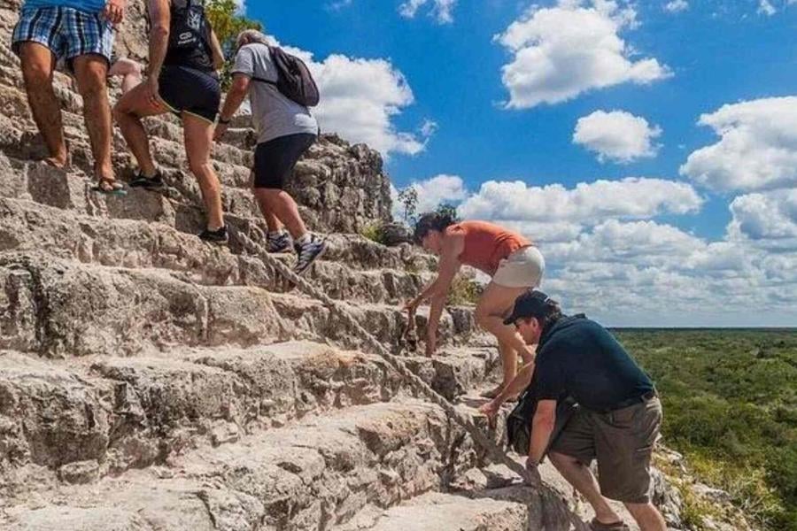 Visitors carefully climb steep stone steps for a rewarding view of the vast jungle landscape.