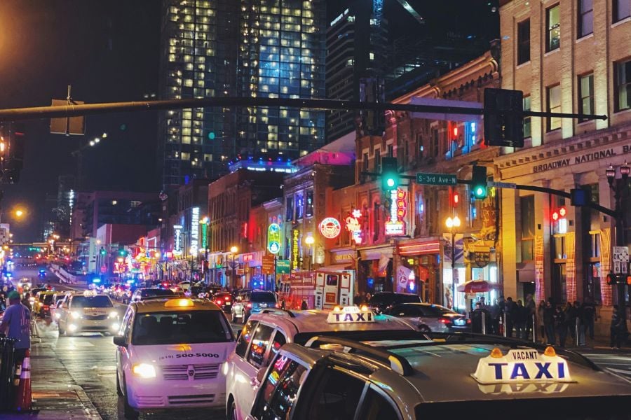 Taxis line up under neon lights on a busy Nashville street at night.