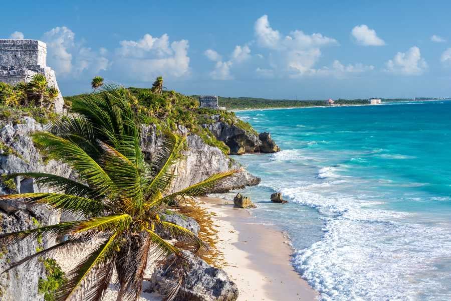  Ancient stone ruins overlooking a stunning turquoise beach framed by swaying palm trees.