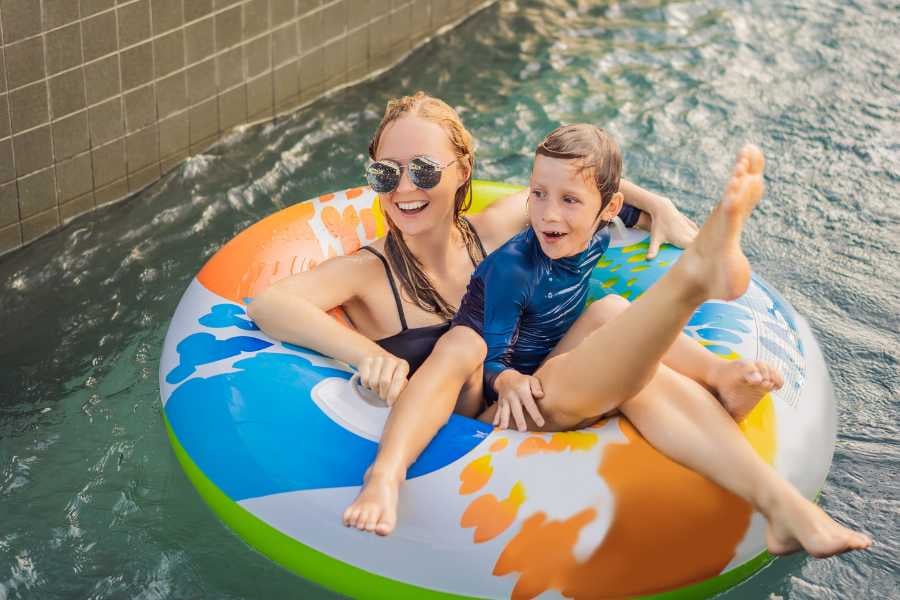 A mother and child relax and laugh while floating on a colorful inner tube in a tranquil pool.